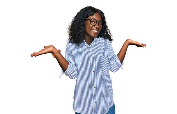 Beautiful african young woman wearing casual clothes and glasses smiling showing both hands open palms, presenting and advertising comparison and balance  - Fotografie, Obrázek