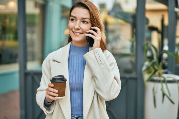 Giovane donna ispanica che parla sullo smartphone e beve caffè in città. - Foto, immagini