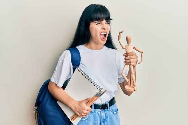 Fiatal spanyol művész diák lány kezében fa próbababa és notebook dühös és őrült sikoltozó frusztrált és dühös, kiabál a harag. düh és agresszív koncepció.  - Fotó, kép