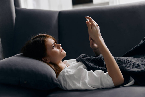 mujer bajo las fundas en el sofá y el teléfono móvil en la mano - Foto, Imagen