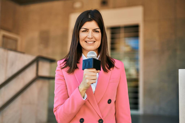 Középkorú riporter nő kezében mikrofon csinál televíziós beszéd szabadban - Fotó, kép