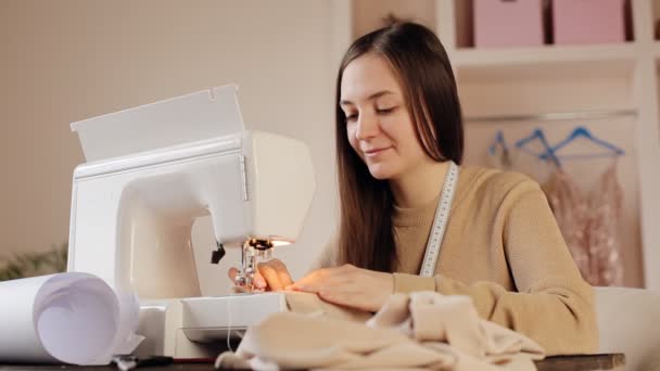 Mujer joven haciendo ropa usando máquina de coser. Sentada en su lugar de trabajo en casa - Metraje, vídeo