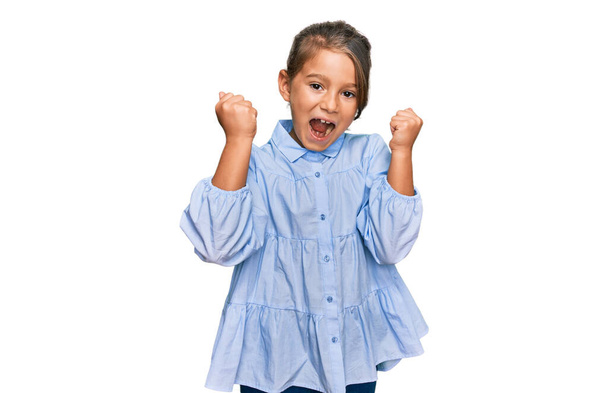 Маленька красива дівчинка в повсякденному одязі кричить гордо, святкуючи перемогу і успіх дуже схвильована піднятими руками
  - Фото, зображення