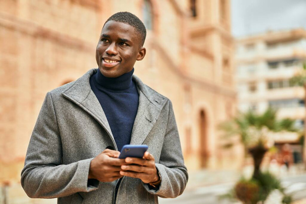 Jovem afro-americano sorrindo feliz usando smartphone na cidade - Foto, Imagem