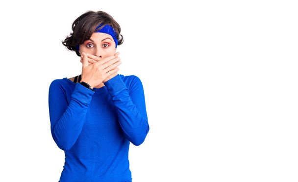 Beautiful young woman with short hair wearing training workout clothes shocked covering mouth with hands for mistake. secret concept.  - Photo, Image