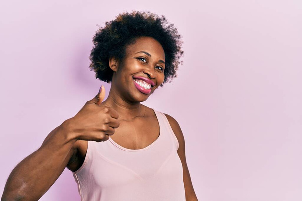 Mladá Afroameričanka v neformální tričku bez rukávů dělá šťastné gesto rukou nahoru. schválení výrazu při pohledu na fotoaparát, který vykazuje úspěch.  - Fotografie, Obrázek