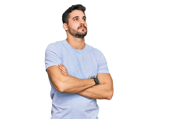 Jeune homme hispanique portant des vêtements décontractés regardant sur le côté avec les bras croisés convaincu et confiant  - Photo, image