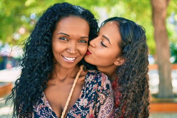 Αφροαμερικανή μητέρα και κόρη χαμογελούν χαρούμενες αγκαλιές και φιλιά στο πάρκο. - Φωτογραφία, εικόνα