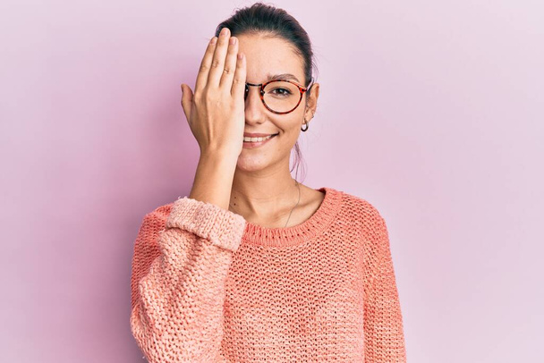 Young caucasian woman wearing casual clothes and glasses covering one eye with hand, confident smile on face and surprise emotion.  - Foto, immagini