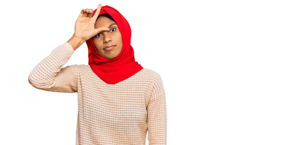 若いですアフリカ系アメリカ人女性身に着けています伝統的なイスラムヒジャーブスカーフ作り楽しいです人々とともに指で額を行います負け犬のジェスチャーモックと侮辱.  - 写真・画像