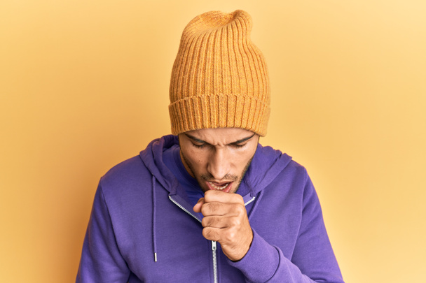 ウールの冬の帽子をかぶっている若いハンサムな男は具合が悪く感じ、風邪や気管支炎の症状として咳をする。ヘルスケアの概念.  - 写真・画像