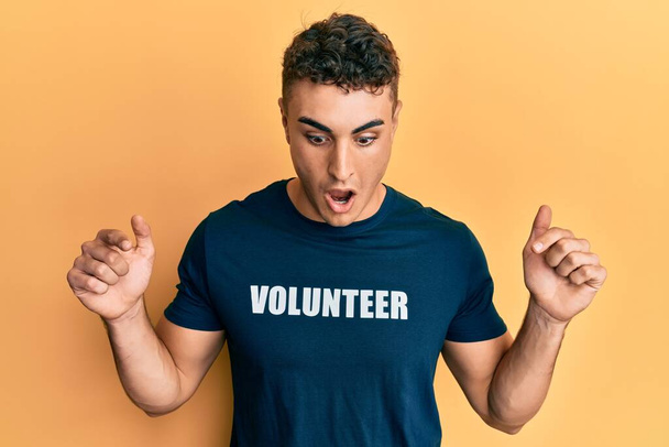 Іспанський молодий чоловік у добровільній сорочці вказує пальцями на рекламу, здивоване обличчя і відкритий рот.  - Фото, зображення