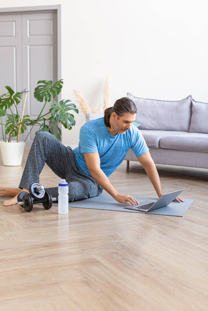 Verticale foto van een man op zoek naar oefening routines online. Home online workout. - Foto, afbeelding