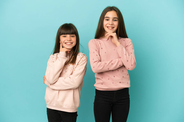 Μικρές αδελφές κορίτσια απομονωμένες σε μπλε φόντο χαμογελώντας με μια γλυκιά έκφραση - Φωτογραφία, εικόνα