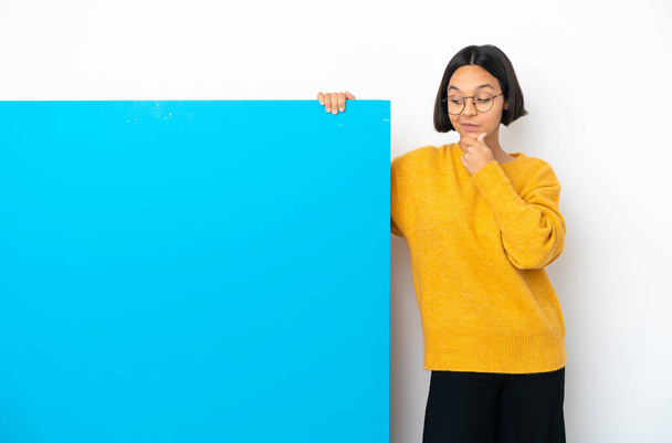 Молодая женщина смешанной расы с большим голубым плакатом на белом фоне думает об идее, глядя вверх - Фото, изображение