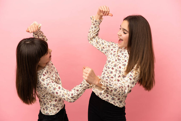 Irmãzinhas meninas isoladas no fundo rosa comemorando uma vitória na posição de vencedora - Foto, Imagem