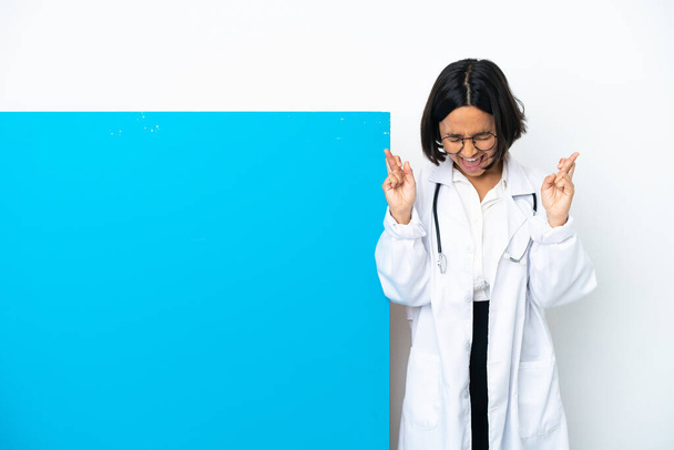 Young mixed race doctor woman with a big placard isolated on white background with fingers crossing - Foto, Imagem