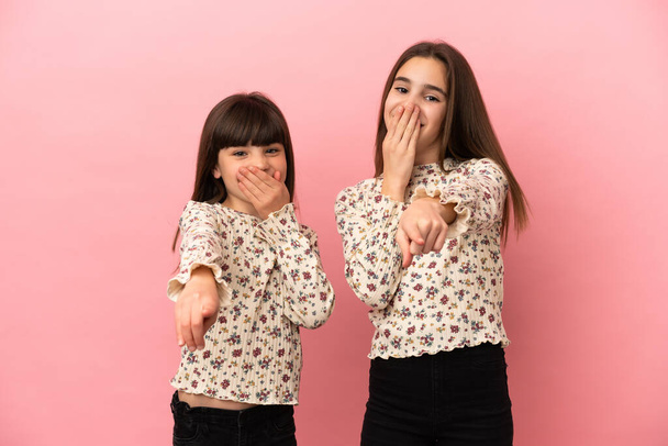Młodsze siostry dziewczyny odizolowane na różowym tle wskazując palcem na kogoś i śmiejąc się - Zdjęcie, obraz