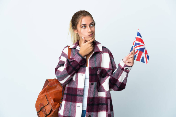 Fiatal nő kezében egy brit zászló elszigetelt fehér háttérrel kétségek és gondolkodás - Fotó, kép