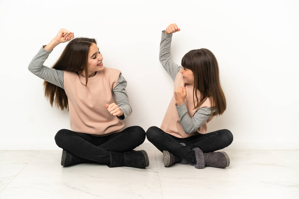 Little sisters sitting on the floor isolated on white background celebrating a victory in winner position - Fotoğraf, Görsel