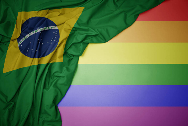 ondeando colorida bandera nacional de Brasil en un fondo de bandera de arco iris gay. - Foto, Imagen