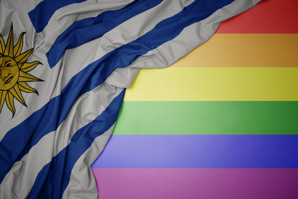 agitant drapeau national coloré de uruguay sur un fond de drapeau arc-en-ciel gay. - Photo, image