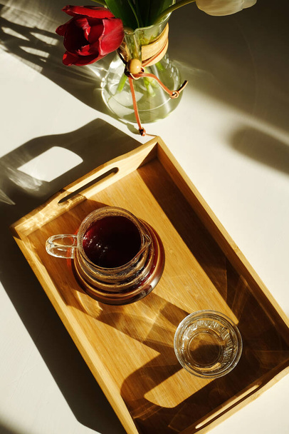 Специальность эстетика кофе третьей волны. Свежезаваренный кофе подается на деревянном бамбуковом подносе на солнечном белом столе. Цветы в кофейном графине - Фото, изображение