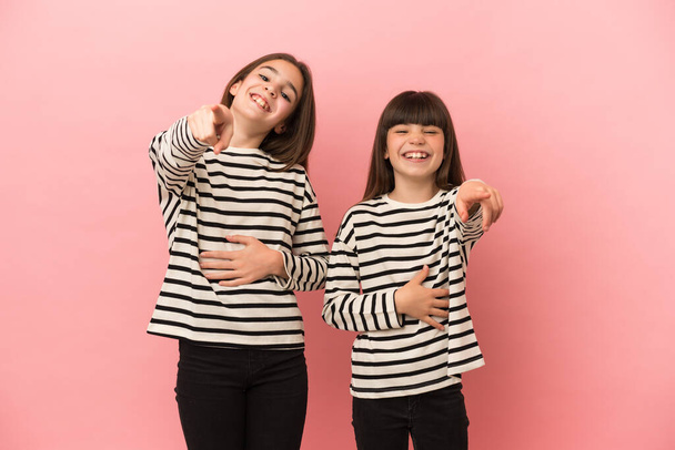 Młodsze siostry dziewczyny odizolowane na różowym tle wskazując palcem na kogoś i śmiejąc się dużo - Zdjęcie, obraz