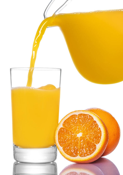 Orange juice pouring from pitcher into glass, isolated on white background. - Photo, Image