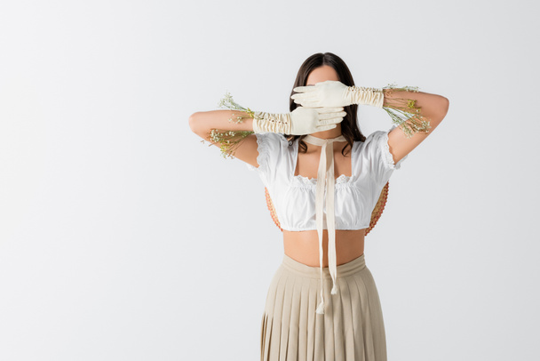 brunette woman covering face with hands in gloves with flowers isolated on white - Photo, Image