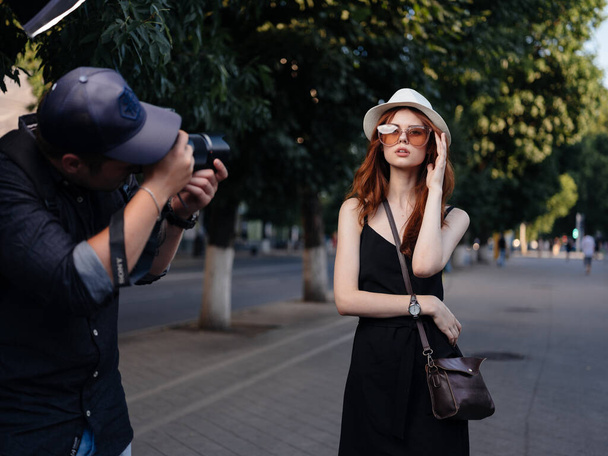 Fashionable Woman in a black dress and in a white hat are resting in nature on the street in the park - Фото, изображение