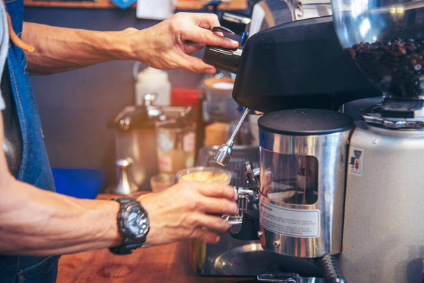 A kávéfőző kávéfőző forró pohárból készít eszpresszót. Cappuccino tejjel az olasz kávézóban. A barista gép közeli kezei készítenek barna tejeskávét a vendég menzának. - Fotó, kép