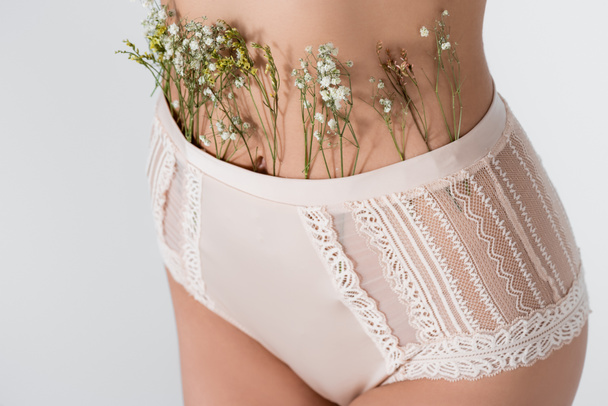 partial view of young woman in panties with blooming flowers isolated on white - Fotó, kép