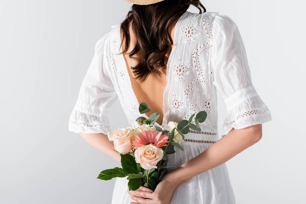 καλλιεργημένη άποψη της νεαρής γυναίκας με φόρεμα κρατώντας μπουκέτο από ανοιξιάτικα λουλούδια πίσω από την πλάτη απομονώνονται σε λευκό - Φωτογραφία, εικόνα