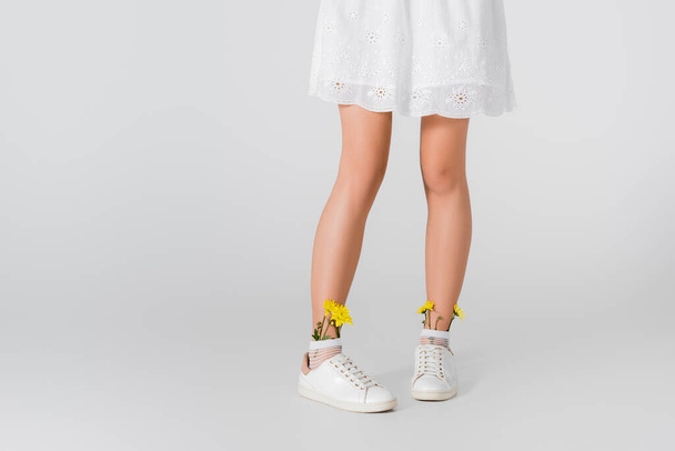 Kırpılmış spor ayakkabılı manken manzarası. Beyaz üzerinde sarı bahar çiçekleri poz veriyor. - Fotoğraf, Görsel