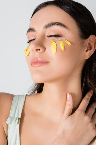 junge Frau mit geschlossenen Augen und gelben Blütenblättern im Gesicht isoliert auf weiß - Foto, Bild