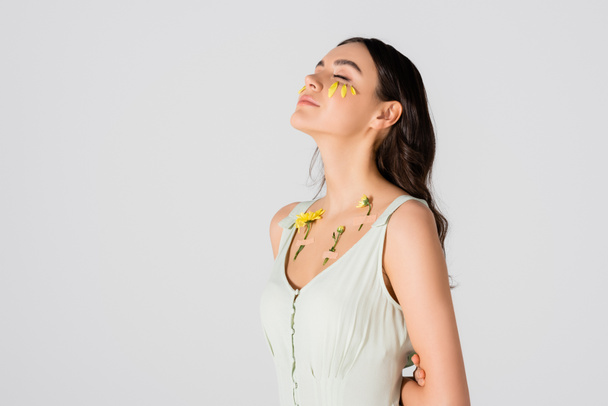 brunetka mladá žena s okvětními lístky na obličeji a omítky se žlutými květy na těle izolované na bílém - Fotografie, Obrázek