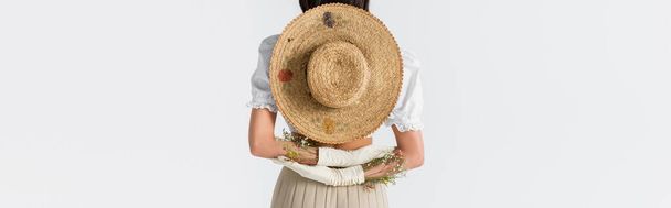 gedeeltelijk zicht van de vrouw in handschoenen met bloemen en strohoed achter de rug geïsoleerd op wit, spandoek - Foto, afbeelding