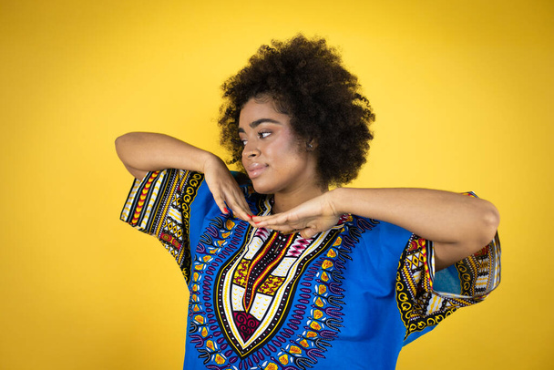 Afričanky americká žena na sobě africké oblečení přes žluté pozadí se šťastnou tváří stojící a usmívající se s sebevědomým úsměvem ukazující zuby - Fotografie, Obrázek