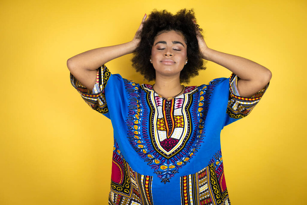 Afro-Amerikalı kadın, sarı arka plan üzerine Afrikalı giysiler giymiş mutlu bir yüzü olan, kendine güvenen bir gülümsemeyle dişlerini gösteren. - Fotoğraf, Görsel