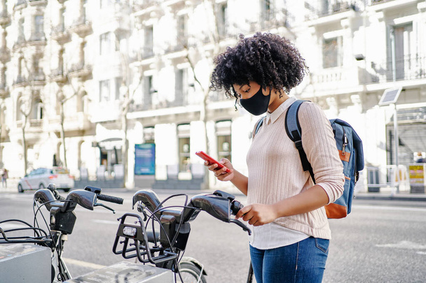 Mujer afroamericana usando su teléfono inteligente para pagar un alquiler de bicicletas. Concepto de transporte ecológico - Foto, imagen