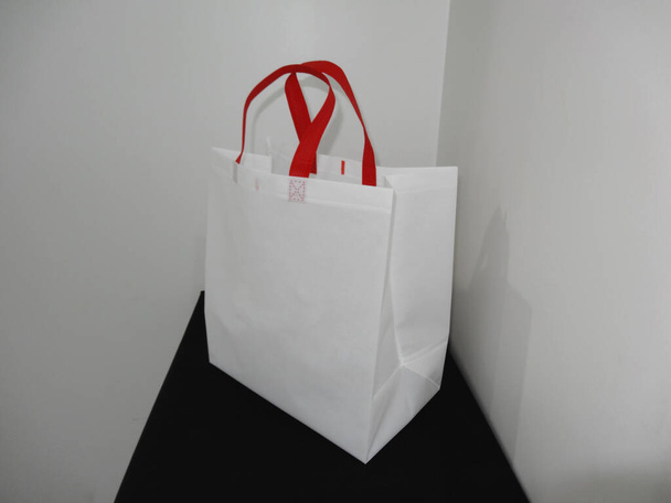 beau sac d'épicerie non tissé blanc avec boucle poignée rouge isolé sur table noire sur fond de mur blanc - Photo, image