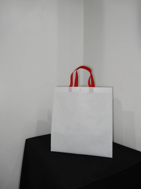schöne Vlies Lebensmittelgeschäft einkaufen weiße Tasche mit roter Henkelschlaufe isoliert auf schwarzem Tisch gegen weißen Wandhintergrund - Foto, Bild