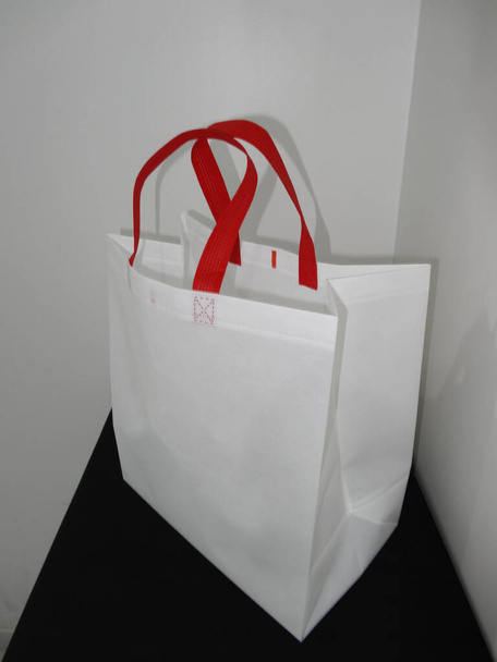 Beautiful Non Woven grocery shopping white bag with red handle loop isolated on black table against white wall background - Foto, Imagen