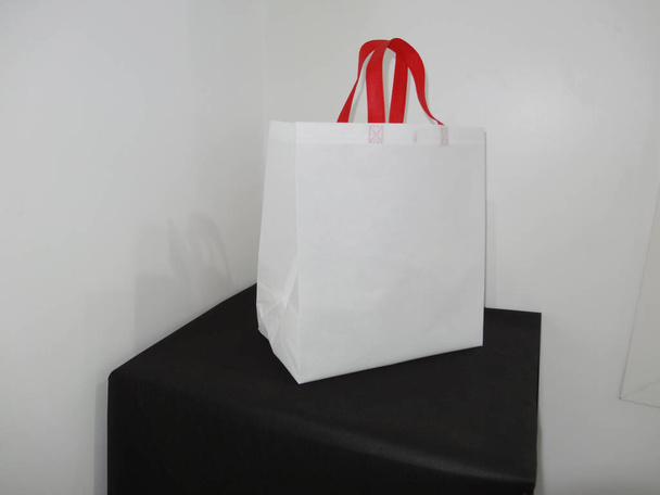 Beautiful Non Woven grocery shopping white bag with red handle loop isolated on black table against white wall background - Foto, afbeelding