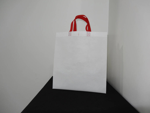 Красиві неткані продуктові покупки білий мішок з червоною петлею ручки ізольовані на чорному столі на білому тлі стіни
 - Фото, зображення