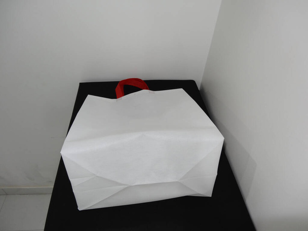Beautiful Non Woven grocery shopping white bag with red handle loop isolated on black table against white wall background - 写真・画像