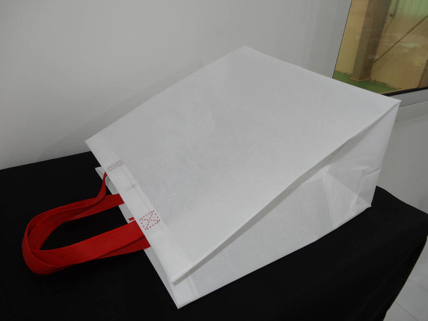 schöne Vlies Lebensmittelgeschäft einkaufen weiße Tasche mit roter Henkelschlaufe isoliert auf schwarzem Tisch gegen weißen Wandhintergrund - Foto, Bild