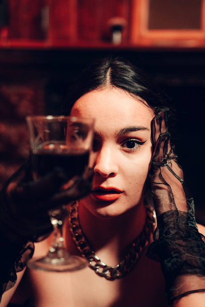 A portrait of a young sexy woman holding a glass of red wine wearing long fashionable gloves in an artificially lit room - Fotoğraf, Görsel