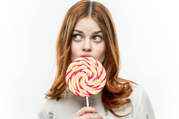 pretty red-haired woman with multicolored lollipop near face cropped view of sweets emotions - Fotó, kép